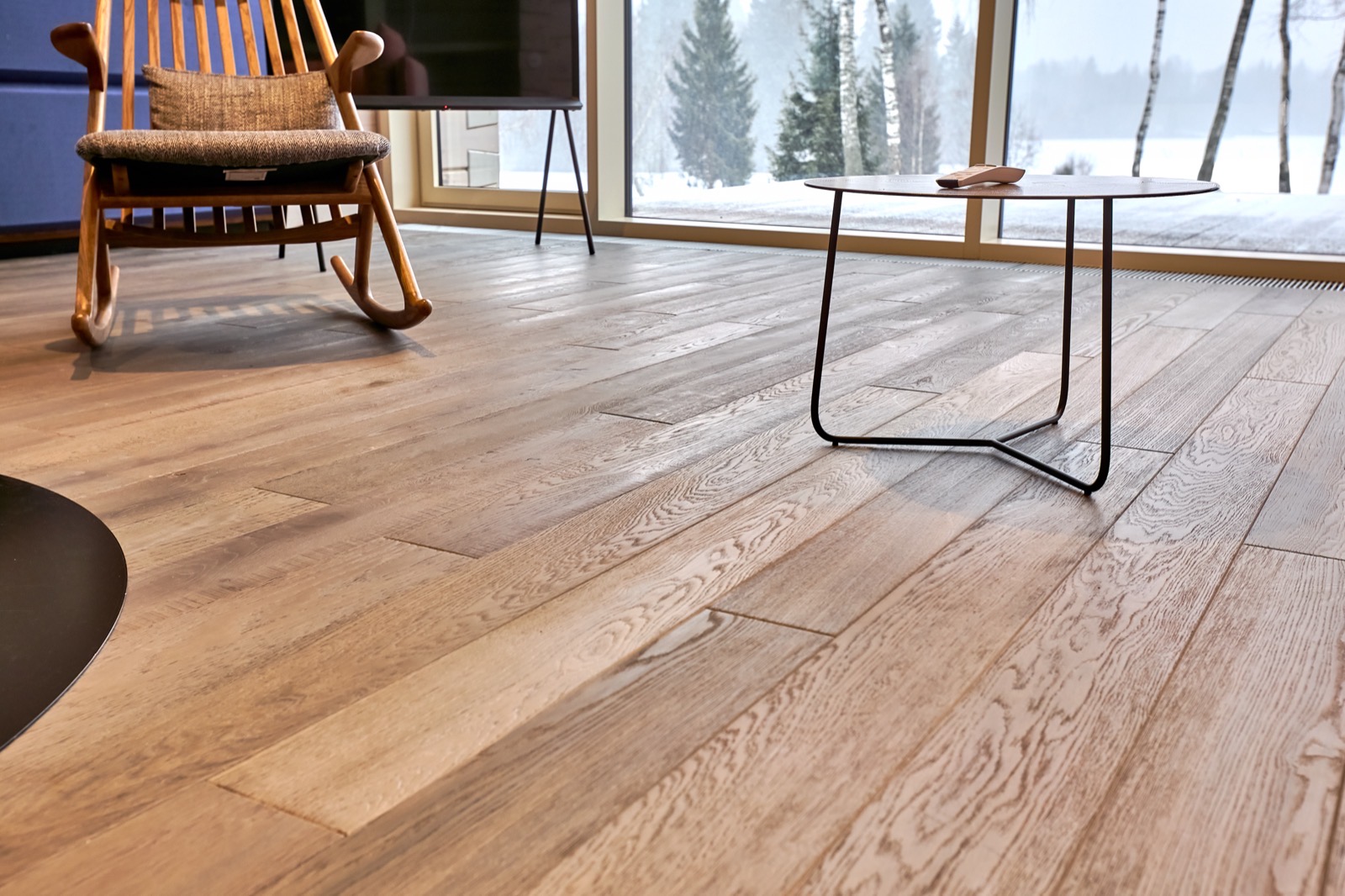 Oak hardwood floor in a living room with a snowy winter landscape outside the window